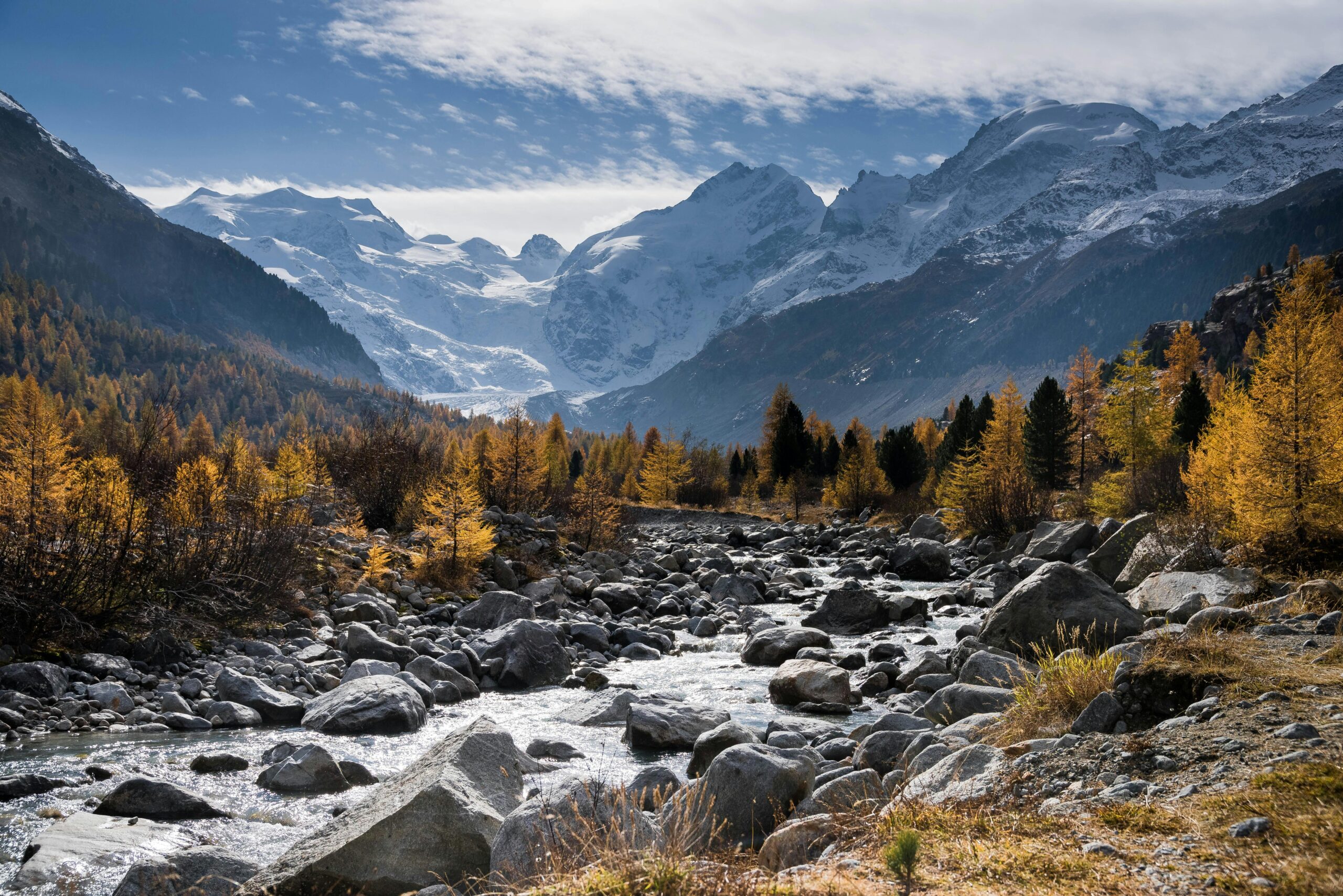 Beautiful autumn landscape of a rocky stream with snowy mountain peaks in the background.